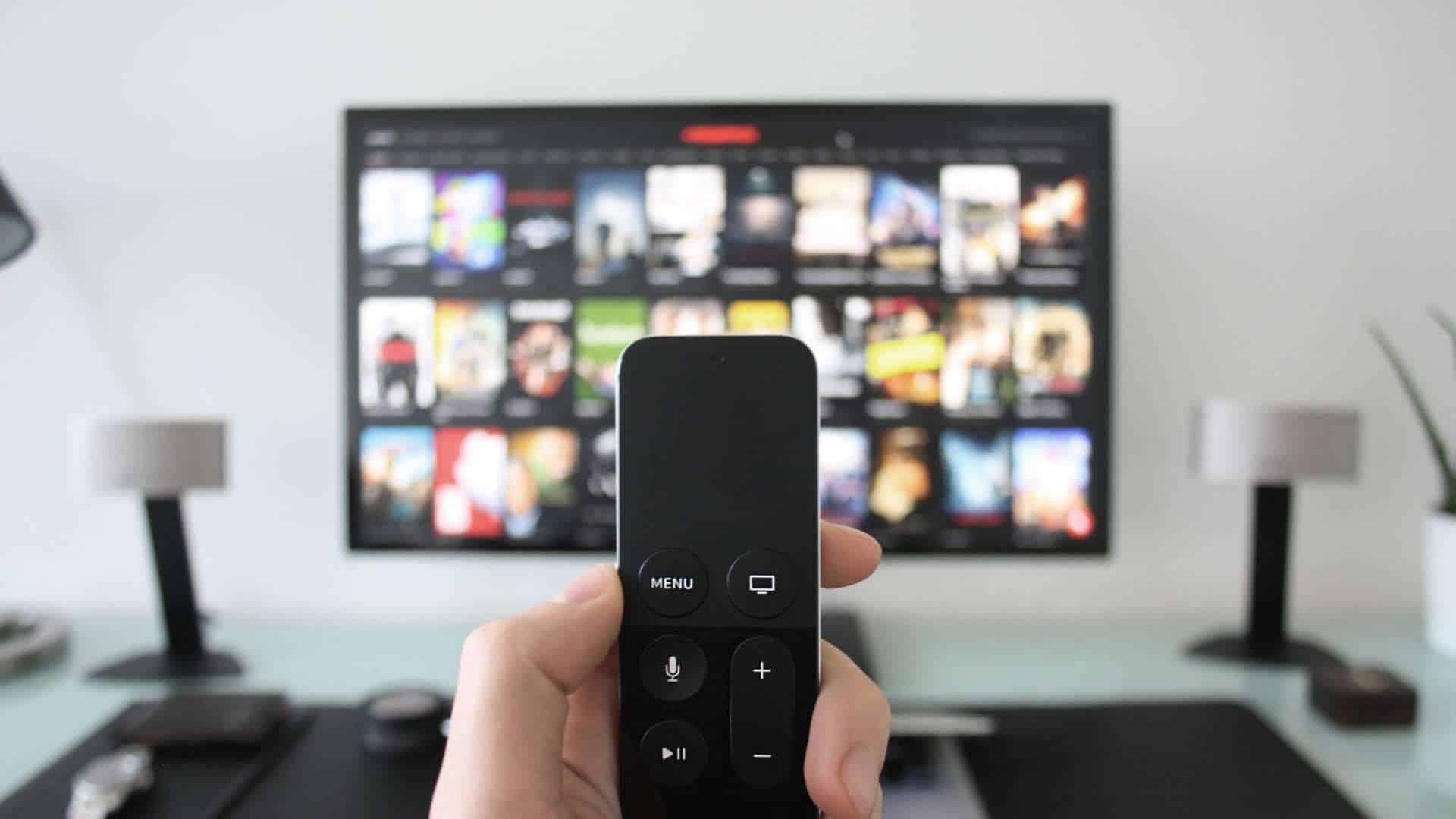 A hand holding a remote in front of a large screen smart tv