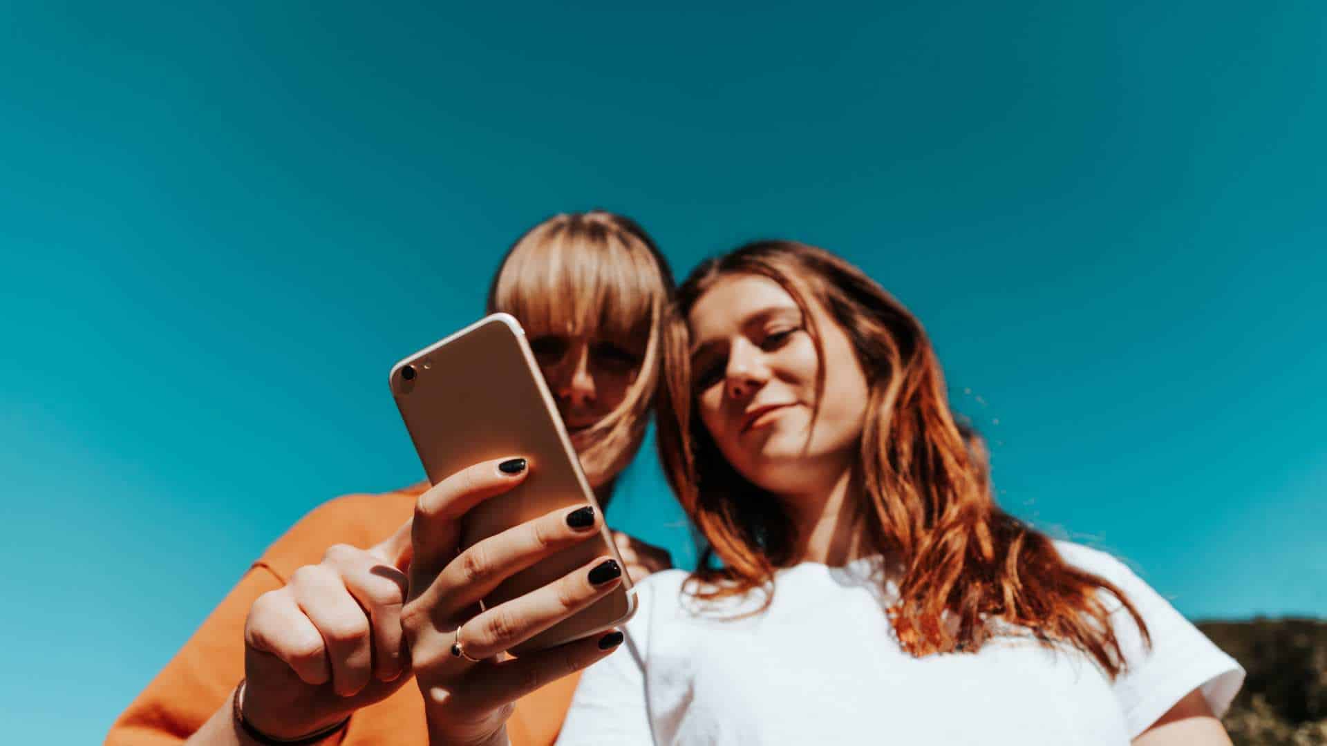 Two women looking at a phone with a blue sky backgound