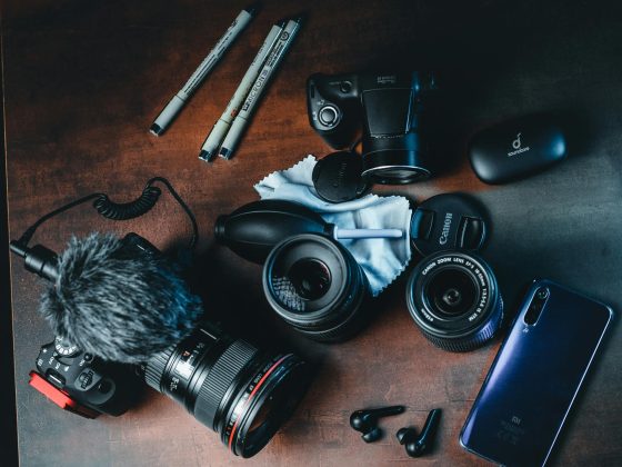 A collection of high-quality photography and video gear on a dark wood surface, showcasing the equipment used for modern multi-channel content creation.