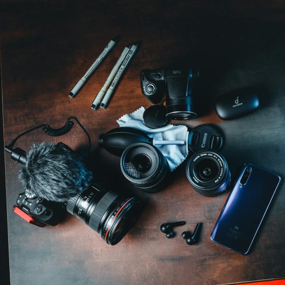 A collection of high-quality photography and video gear on a dark wood surface, showcasing the equipment used for modern multi-channel content creation.