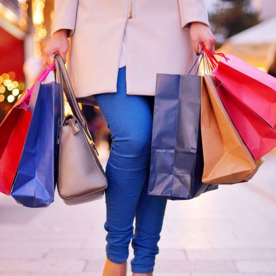 A woman end of year shopping in a mall with handfulls of shopping bags.