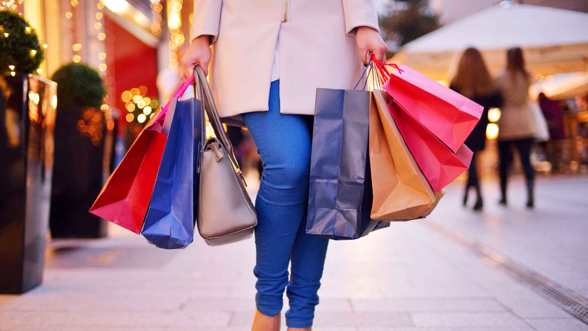 A woman end of year shopping in a mall with handfulls of shopping bags.